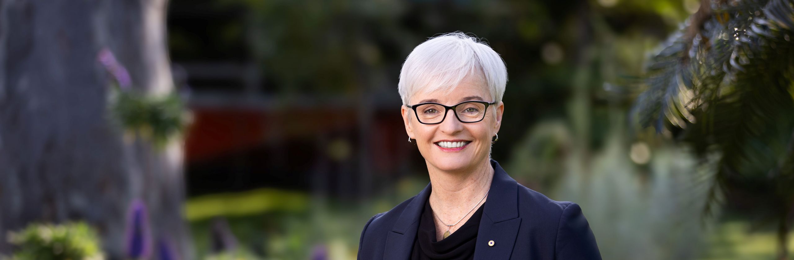 Professor Emma Johnston in navy suit in front of garden smiling at camera.