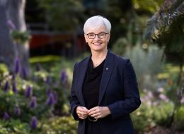 Professor Emma Johnston in navy suit in front of garden smiling at camera.