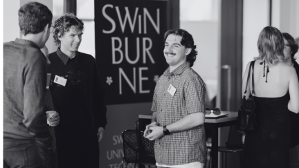 Candid photograph of man in checkered shirt conversing with other scholars.