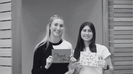 Two scholars looking at the camera with handwritten thank you signs.