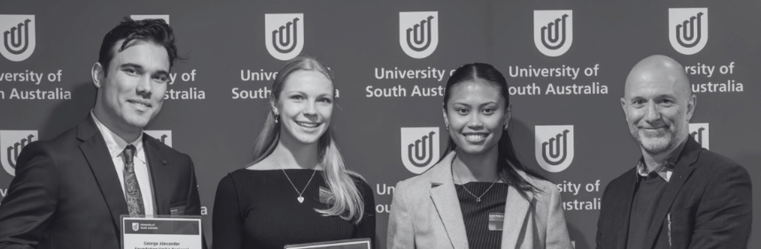 Three scholarship recipients posing with program manager facing camera, holding certificates.