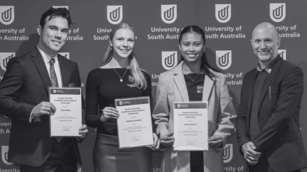 Three scholarship recipients posing with program manager facing camera, holding certificates.