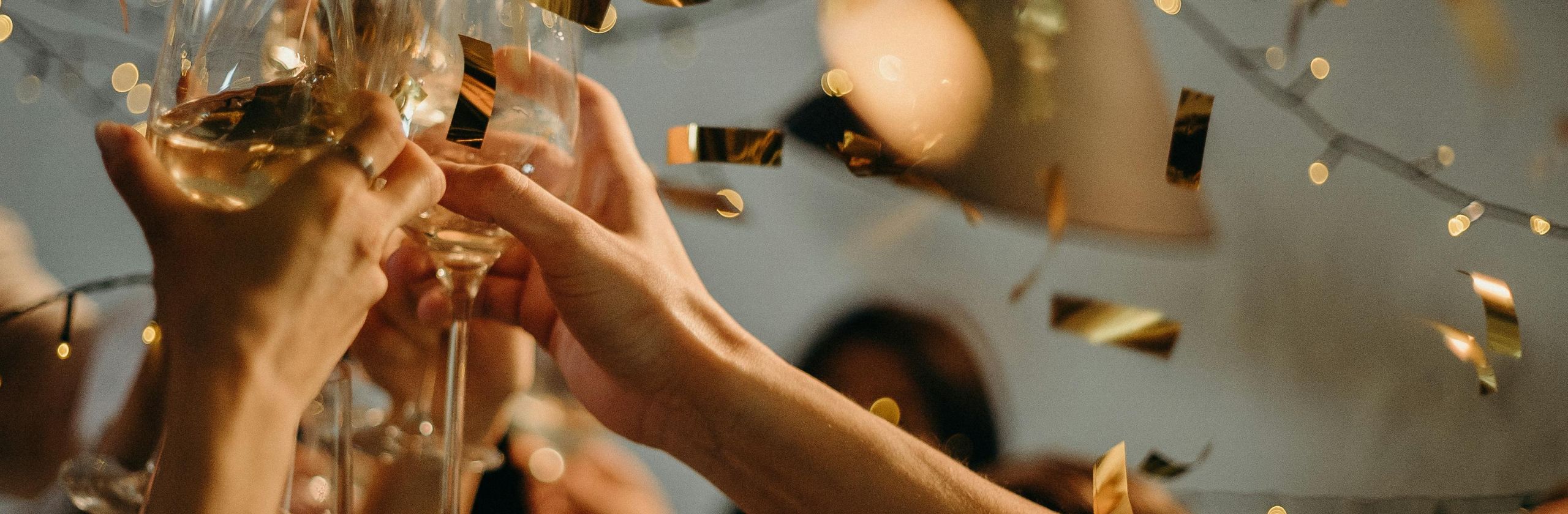 Image of hands clinking wine glasses with confetti in background.