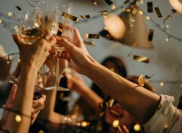 Image of hands clinking wine glasses with confetti in background.